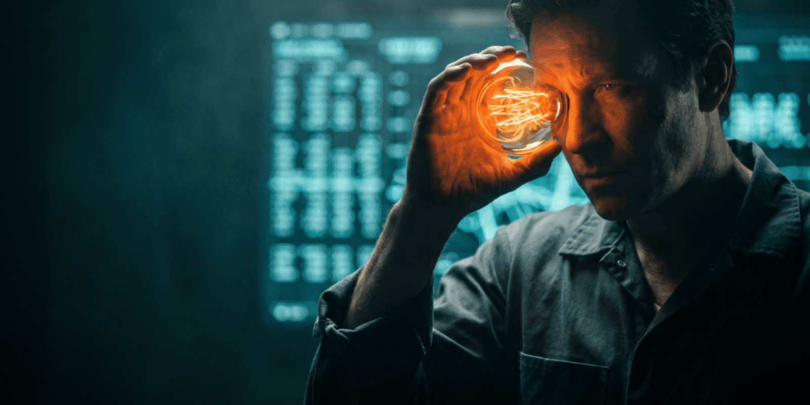 Man holding glowing light bulb to his temple in a tech-themed setting.