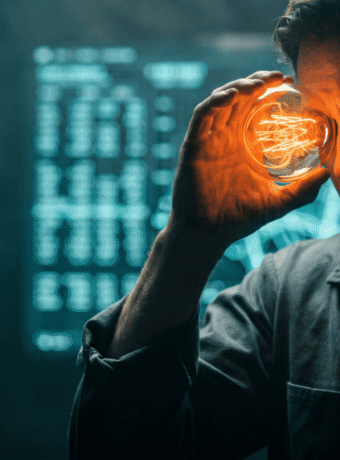 Man holding glowing light bulb to his temple in a tech-themed setting.