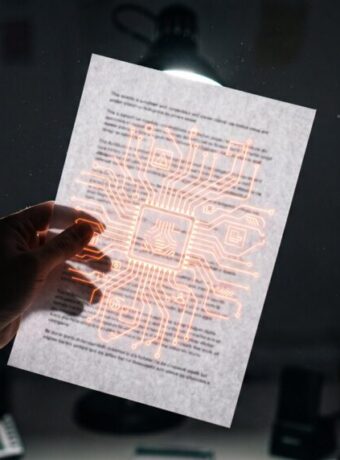 Person holding a paper with digital circuit design glowing in a dark room.