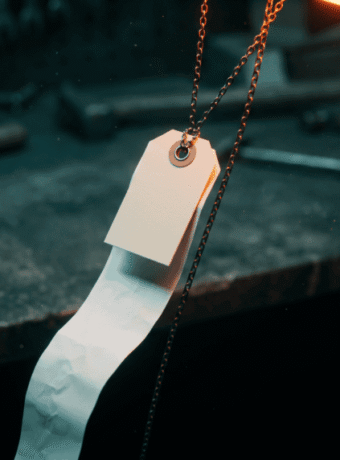 A blank price tag hanging on a chain above a workbench with a long paper receipt unspooling into shadow, illustrating the real cost of AI software for small business