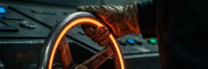 Close-up of a hand gripping a glowing orange wheel in an industrial setting.