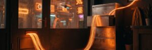 A ribbon of orange light pours through a shop door's mail slot, crosses the floor into an open steel cabinet drawer, and slips out a cracked window into a neon city at night