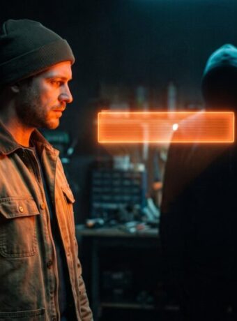 Man in a beanie facing a hacker in a dark workshop with glowing digital effects.