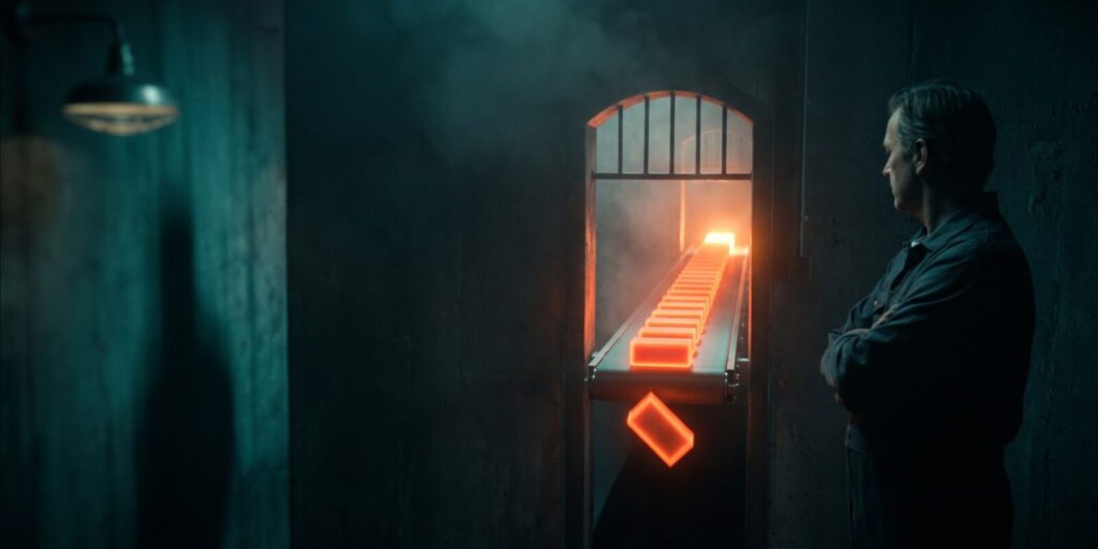 Man observing a glowing orange conveyor belt in a dark industrial setting.